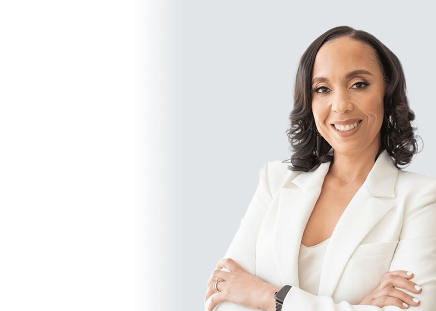 Smiling woman in black dress with plant backdrop.