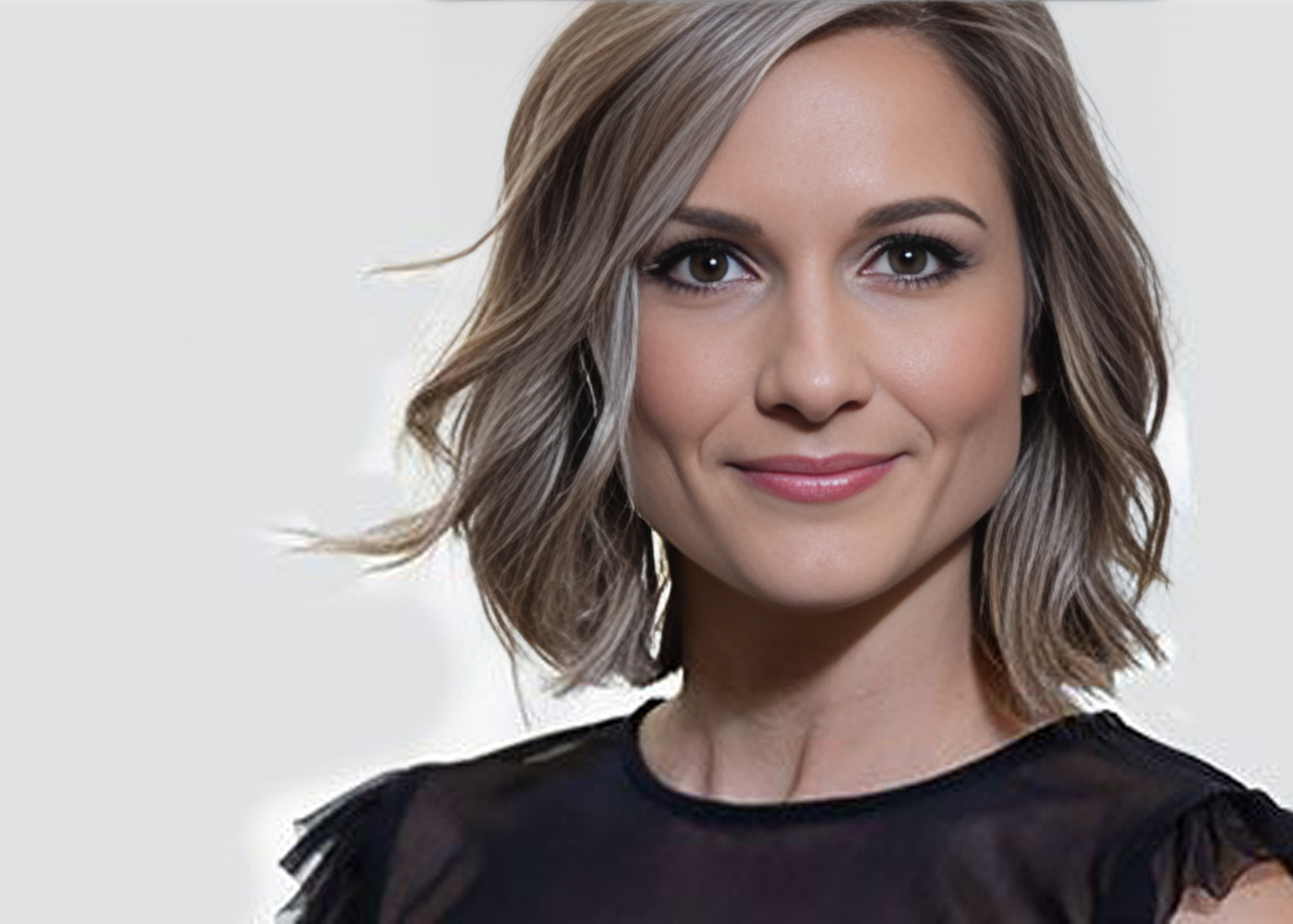 Smiling woman in black dress with plant backdrop.