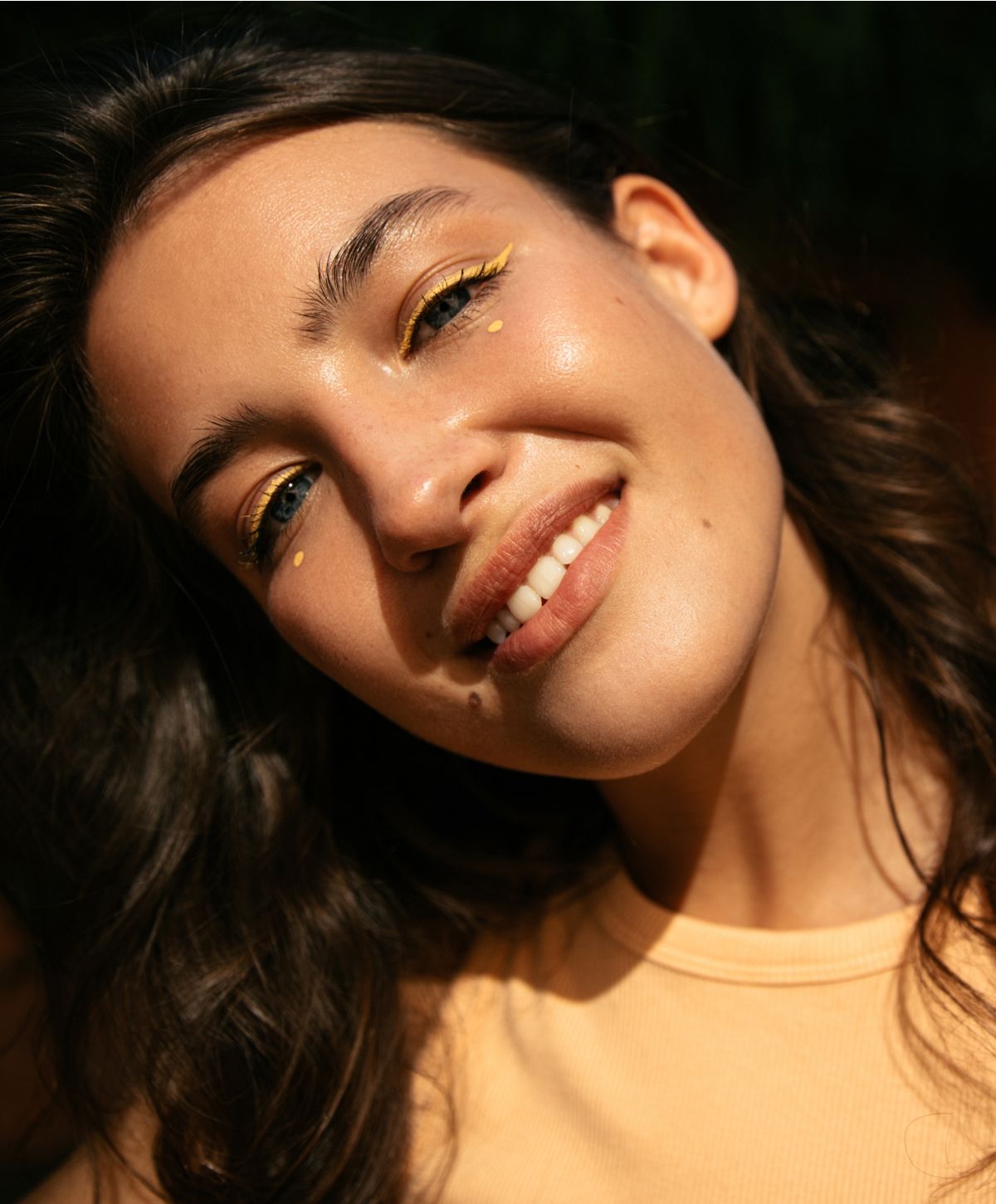 Smiling woman with yellow eye makeup and sunshine.