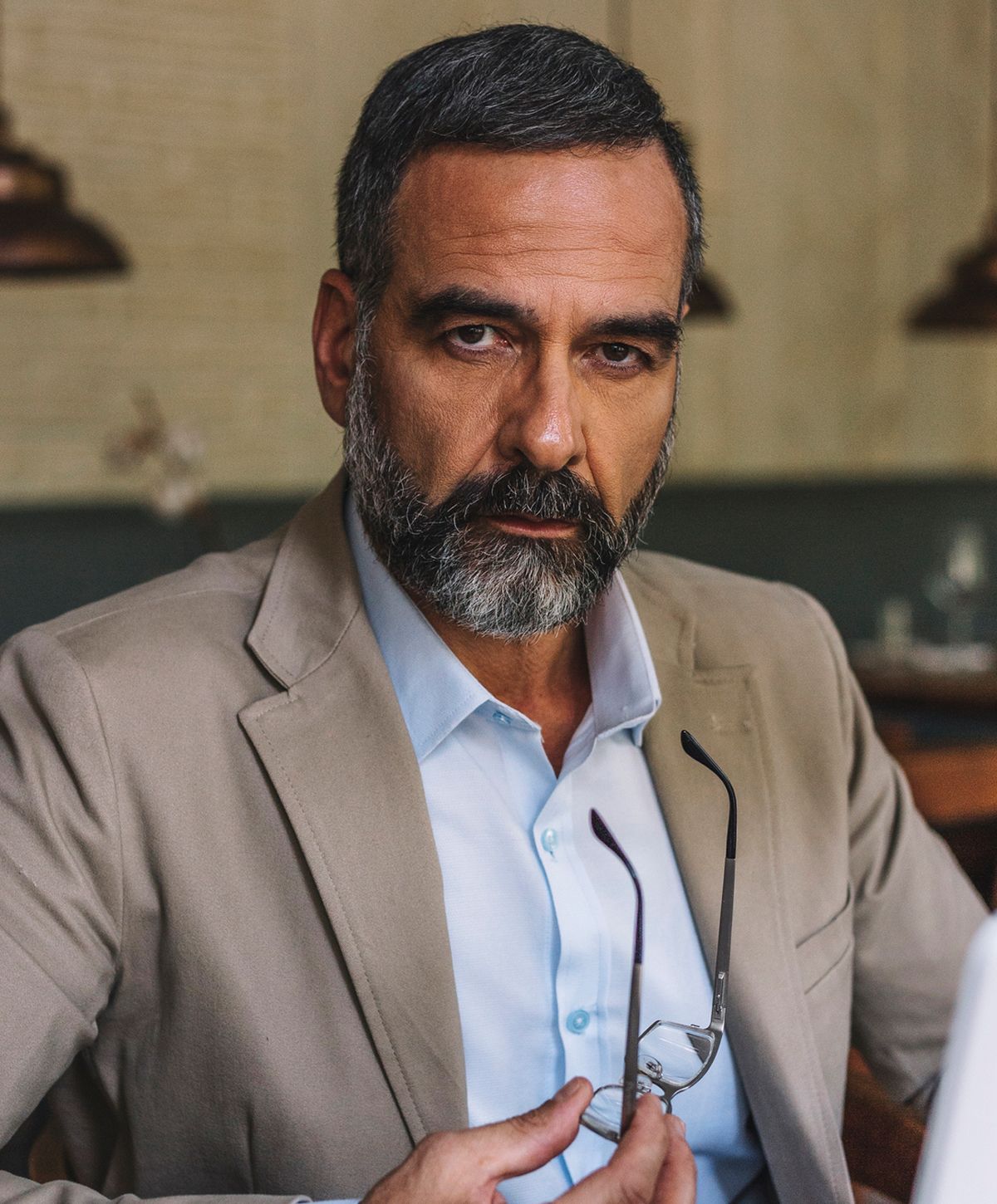 Man holding glasses, serious expression, stylish suit.