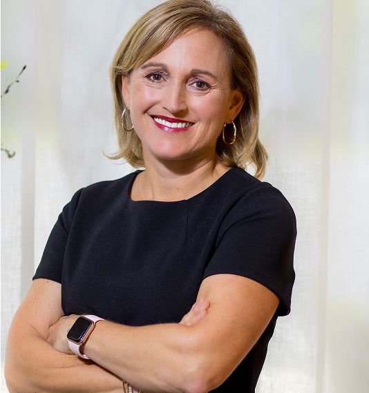 Smiling woman with crossed arms, wearing black dress.