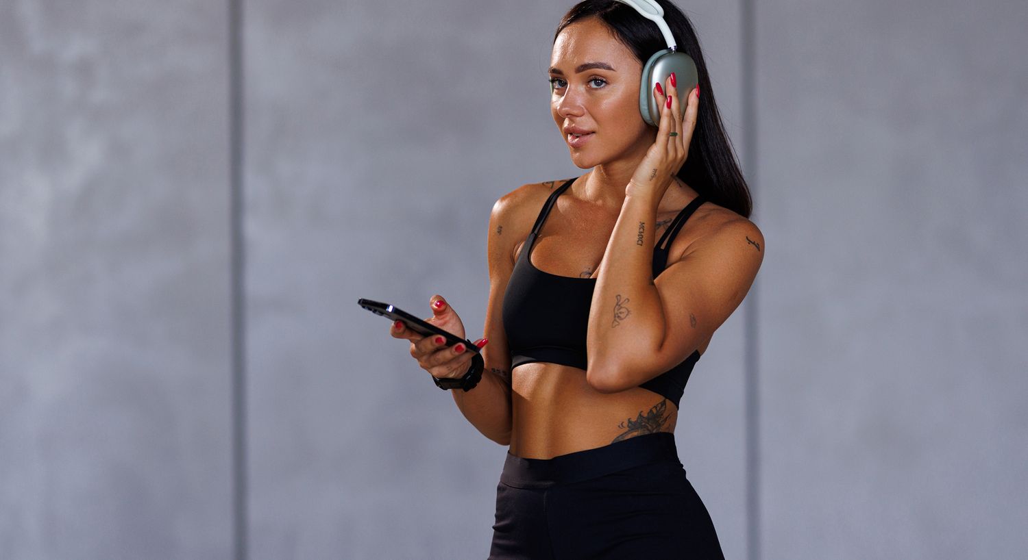 Woman in workout attire with headphones and phone.