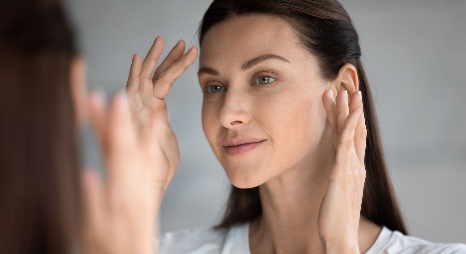 Woman examining her skincare routine in mirror.